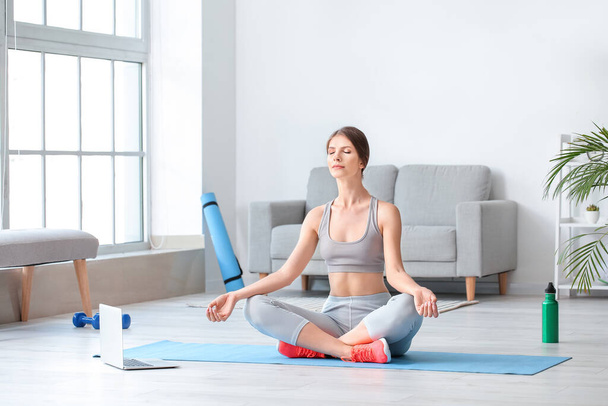 Jovem esportiva com laptop praticando ioga em casa
 - Foto, Imagem