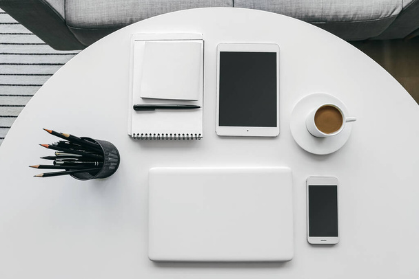 Modern laptop, tablet computer, mobile phone, cup of coffee and stationery on table in room - Photo, Image