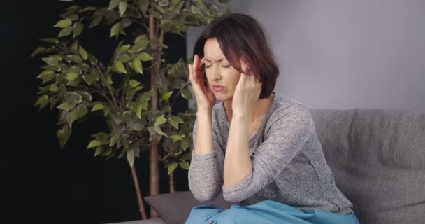 Unhappy woman sitting on couch and feeling strong migraine - Felvétel, videó