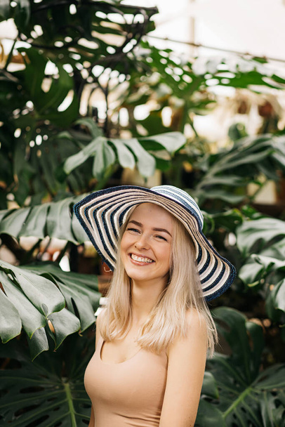 Vertical closeup portrait of happy attractive caucasian young woman with blonde hair, wearing hat, swimsuit, smiling with enjoying sun, relaxing at tropical resort. Summer concept. - Foto, Bild