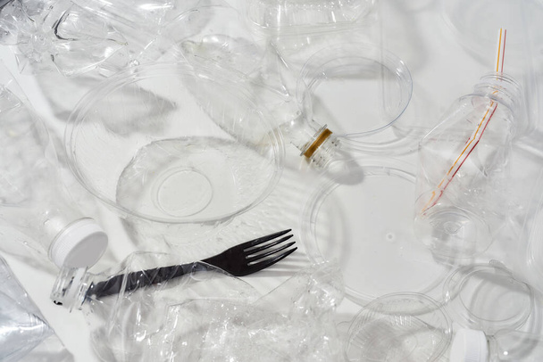 Flatlay composition with used plastic bottles, containers, forks, spoons, egg packaging, caps over white background - Фото, изображение