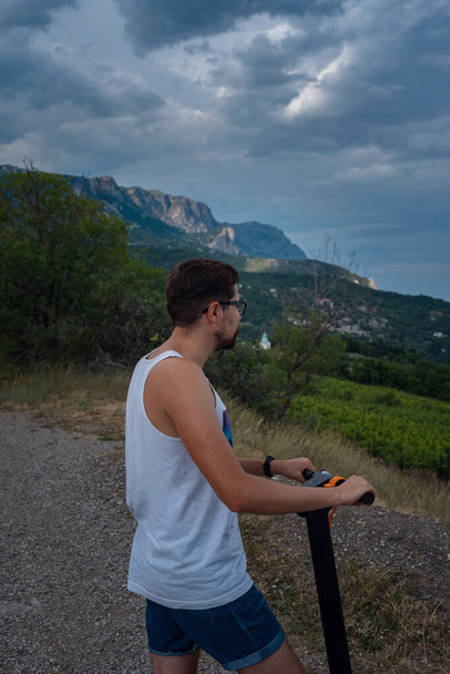 Junger Mann auf einem Elektroroller in den Bergen. genießen Sie frische Luft und schöne Ausblicke. Ökologisches Verkehrskonzept - Foto, Bild
