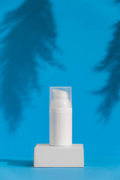 青い背景に白いスキンケア製品チューブ、広告コンセプト。ブランドのための場所とボディスキン治療コンテナ,テキストのためのフリースペース. - 写真・画像