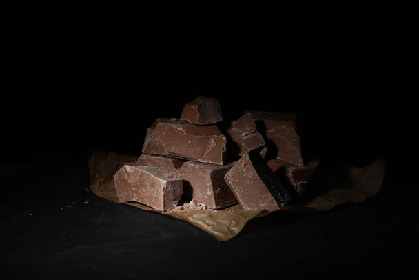 Pieces of tasty milk chocolate on black table, closeup - Zdjęcie, obraz