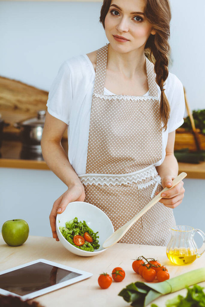 Young brunette woman cooking in kitchen. Housewife holding wooden spoon in her hand. Food and health concept - 写真・画像