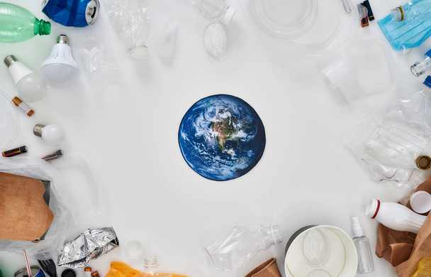 Flatlay composition with different waste, garbage types and paper model of Earth in the center over white background - Photo, Image