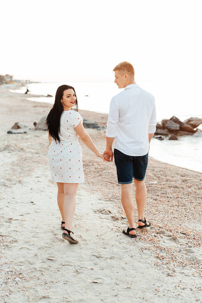 Loving couple in white clothes during a honeymoon at sea walk on the sand at a photoshoot Love Story, ocean coast, beach - Photo, image