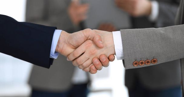 Business people shaking hands while standing with colleagues after meeting or negotiation, close-up. Group of unknown businessmen and women in modern office. Teamwork, partnership and handshake - 写真・画像