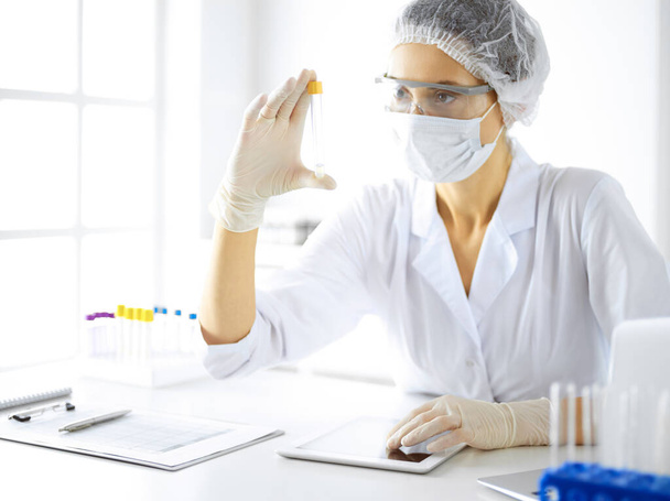 Professional female scientist in protective eyeglasses researching tube with reagents in laboratory. Concepts of medicine and research - Photo, Image
