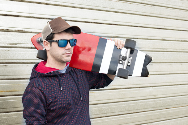 Портрет человека со скейтбордом и солнцезащитными очками на металлическом бэкгре
 - Фото, изображение