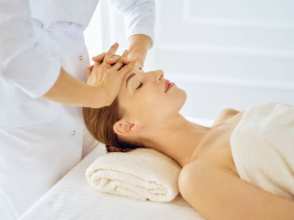 Beautiful woman enjoying facial massage with closed eyes. Spa treatment concept in medicine - Zdjęcie, obraz