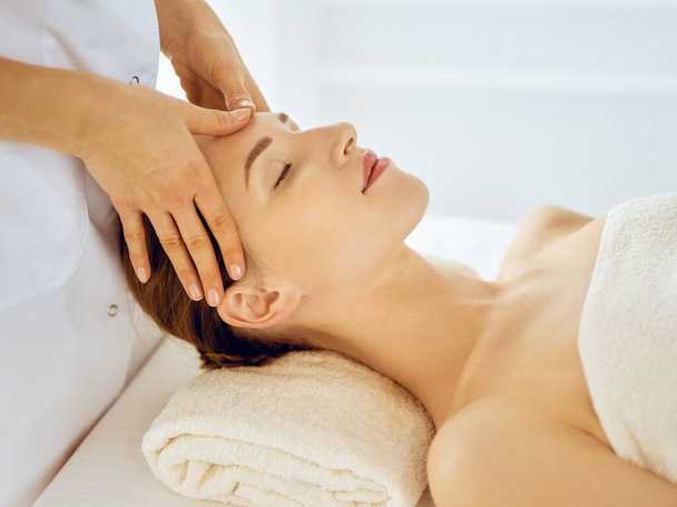 Beautiful woman enjoying facial massage with closed eyes. Spa treatment concept in medicine - Фото, изображение