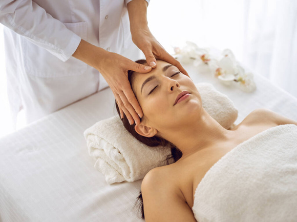 Beautiful brunette woman enjoying facial massage with closed eyes. Relaxing treatment in medicine and spa center concepts - Φωτογραφία, εικόνα