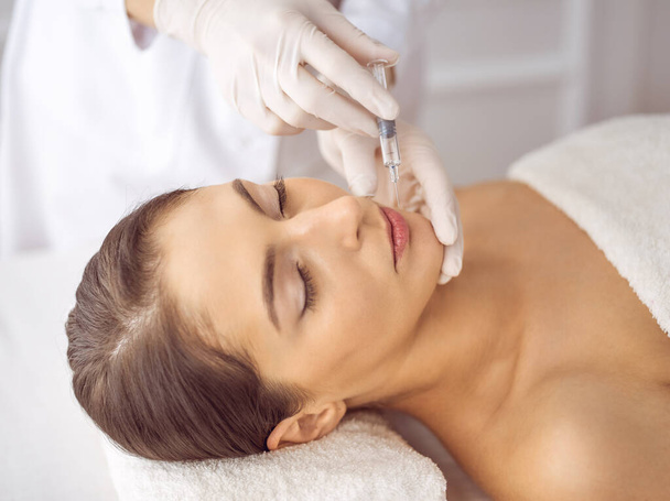 Beautician doing beauty procedure with syringe to face of young brunette woman. Cosmetic medicine and surgery, beauty injections - Valokuva, kuva
