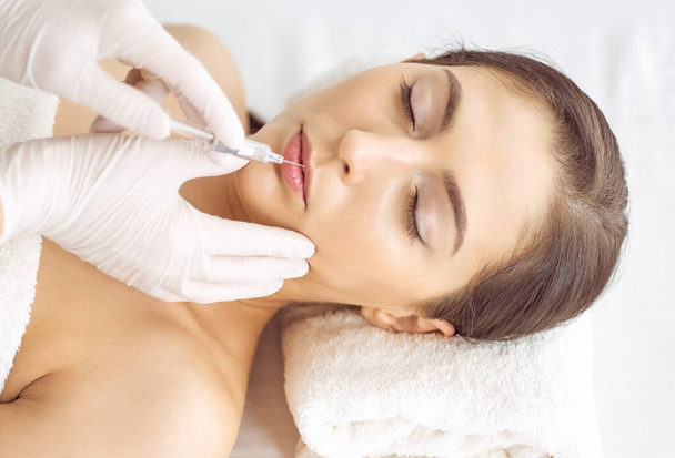 Beautician doing beauty procedure with syringe to face of young brunette woman. Cosmetic medicine and surgery, beauty injections - Valokuva, kuva