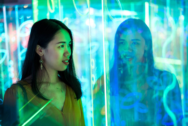 Asian woman portrait lit up by neon illuminated mirrors at night - Фото, изображение