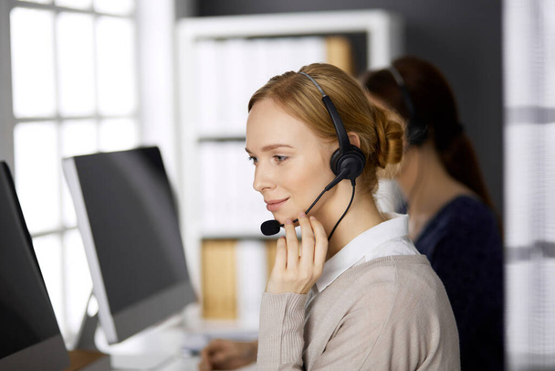 Businesswoman talking by headset while sitting in office. Call center and diverse people group in business - Foto, Bild