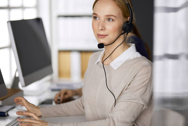 Businesswoman talking by headset while sitting in office. Call center and diverse people group in business - Foto, Imagem
