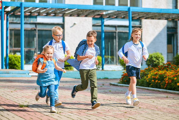 group of school children with backpacks run out of school, after the end of classes. Classmates, school friends. The beginning of holidays. The end of quarantine. Back to school. - Фото, зображення