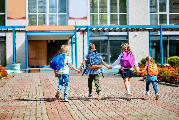 group of school children with backpacks run out of school, after the end of classes. Classmates, school friends. The beginning of holidays. The end of quarantine. Back to school. - Photo, Image