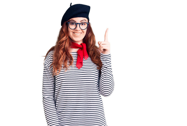 Fiatal gyönyörű nő visel francia megjelenés svájcisapka ujjal felfelé sikeres ötlet. kilépett és boldog volt. Egyes számú..  - Fotó, kép