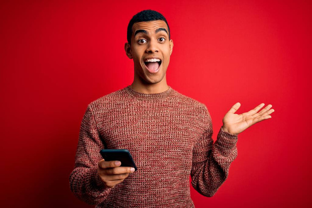 Handsome african american man having conversation using smartphone over red background very happy and excited, winner expression celebrating victory screaming with big smile and raised hands - 写真・画像