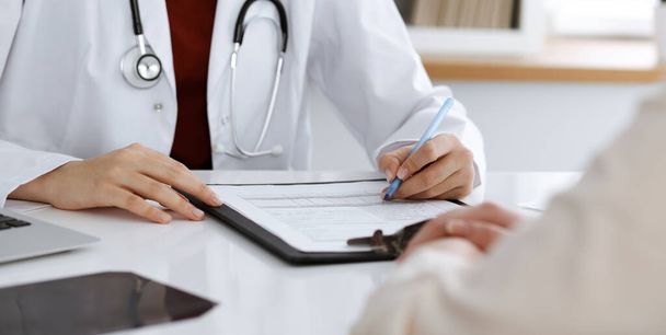 Unknown woman-doctor filling up an application form while consulting patient. Medicine concept - Photo, Image