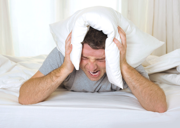 Man suffering hangover and headache with pillow on his head - 写真・画像