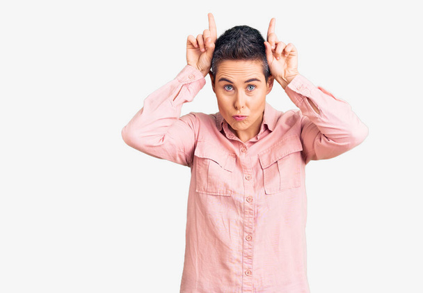Young woman with short hair wearing casual clothes doing funny gesture with finger over head as bull horns  - Photo, Image