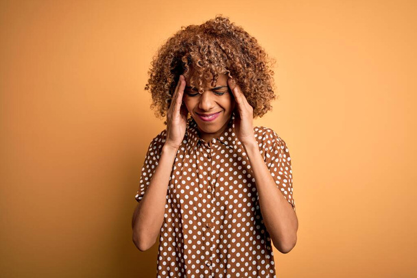 Young beautiful african american woman wearing casual shirt standing over yellow background with hand on head for pain in head because stress. Suffering migraine. - Photo, Image