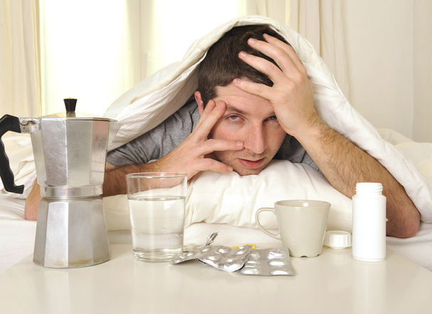 Mann mit Kopfschmerzen und Kater mit Tabletten im Bett - Foto, Bild