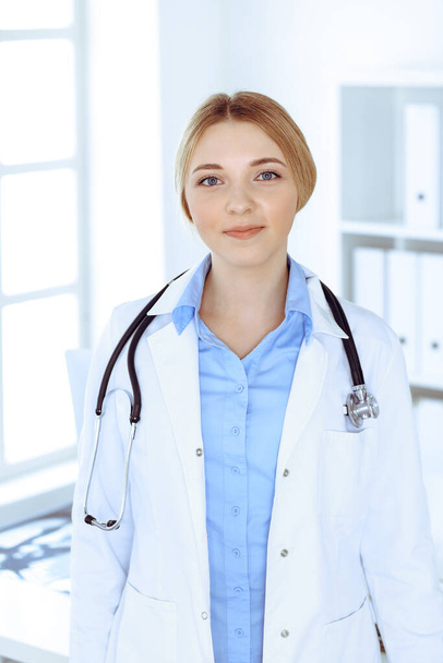 Young woman doctor at work in hospital looking at camera. Blue colored blouse of therapist looks good. Medicine and healthcare concept - Photo, image