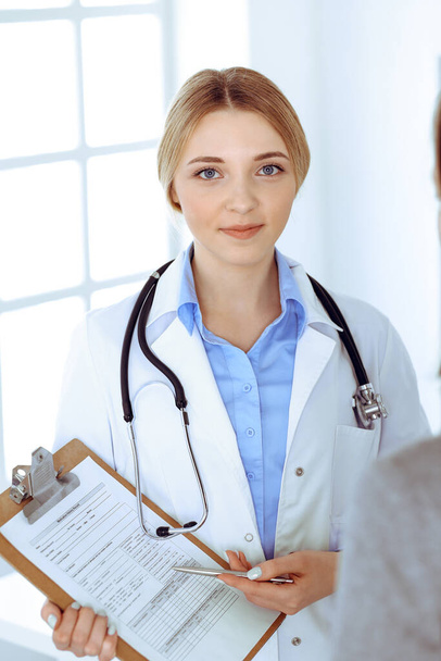 Young woman doctor and patient at medical examination at hospital office. Blue color blouse of therapist looks good. Medicine and healthcare concept - Foto, imagen