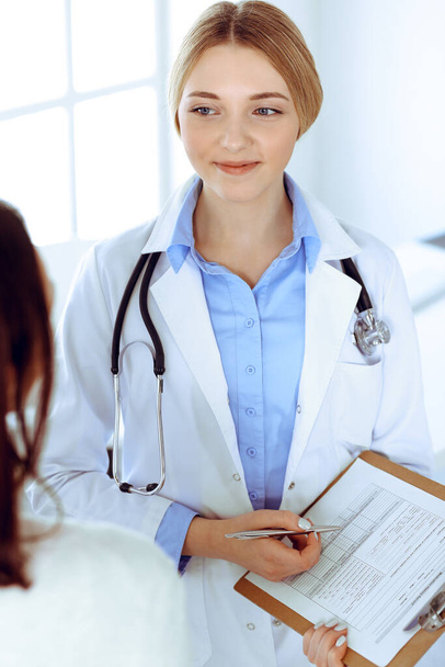 Young woman doctor and patient at medical examination at hospital office. Blue color blouse of therapist looks good. Medicine and healthcare concept - Fotó, kép