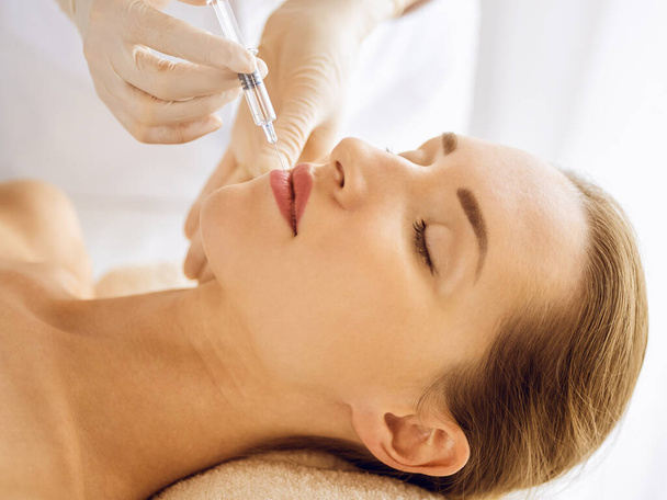 Beautiful woman receiving beauty injections with closed eyes. Beautician doctor hands doing beauty procedure to female face with syringe - Foto, Imagem