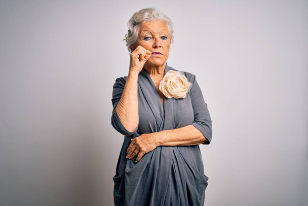 Senior mooie grijs-harige vrouw draagt casual jurk staan over witte achtergrond mond en lippen gesloten als rits met vingers. Geheim en stil, taboe praten - Foto, afbeelding