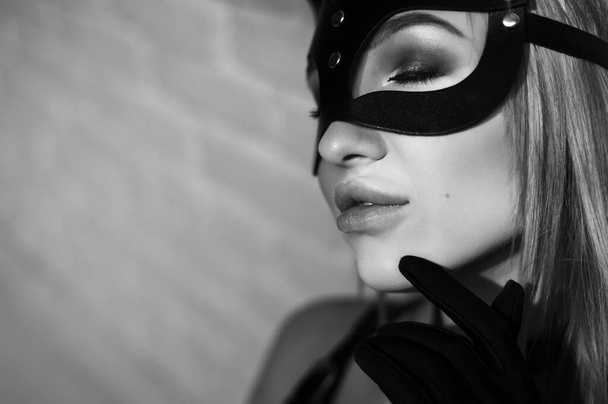 Egy lány fekete farsangi maszkban. Pózol a fekete háttér a stúdióban. - Fotó, kép