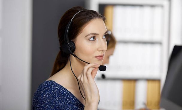 Friendly asian or Latin american businesswoman talking by headset in office. Call center and diverse people group in business - Фото, зображення