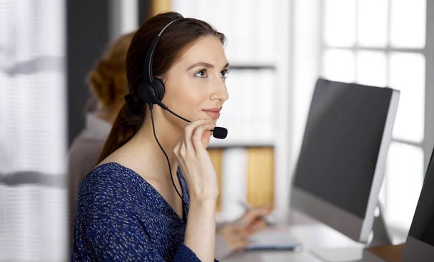 Friendly asian or Latin american businesswoman talking by headset in office. Call center and diverse people group in business - Photo, Image