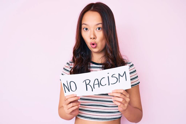 Jovem menina chinesa bonita segurando nenhum banner racismo assustado e espantado com a boca aberta para surpresa, rosto descrença
  - Foto, Imagem