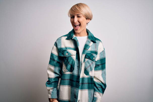 Young blonde woman with short hair wearing casual retro green shirt over isolated background winking looking at the camera with sexy expression, cheerful and happy face. - 写真・画像
