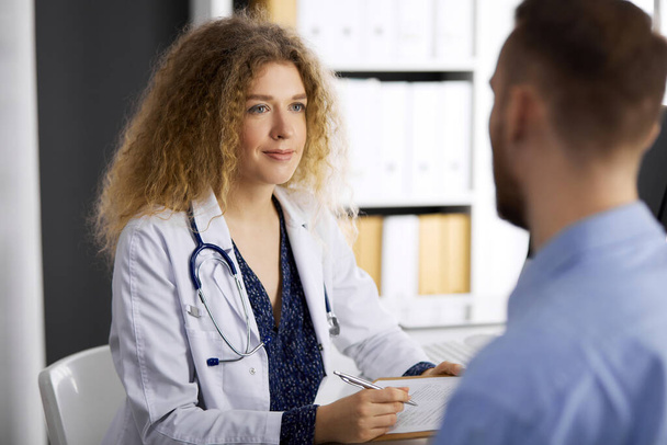 Female doctor and male patient discussing current health examination while sitting in clinic. Perfect medical service and medicine concept - Foto, Imagem