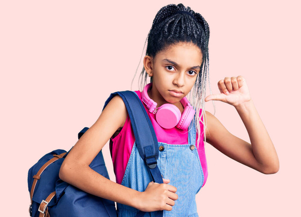 Cute african american girl holding student backpack using backpack with angry face, negative sign showing dislike with thumbs down, rejection concept  - Photo, Image