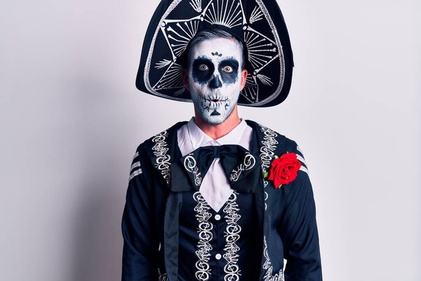Молодой человек, одетый в мексиканский день мертвого костюма поверх белого испуганного и шокированного удивлением выражения лица, страха и возбужденного лица
.  - Фото, изображение