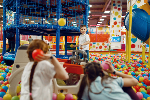 Děti házejí míčky do zábavního centra. Dívky a chlapec volný čas na dovolené, dětské štěstí, šťastné děti na hřišti - Fotografie, Obrázek