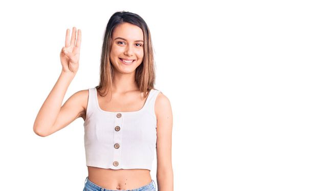 Junge schöne Mädchen tragen legeres ärmelloses T-Shirt und zeigen mit Finger Nummer drei nach oben, während sie selbstbewusst und glücklich lächeln.  - Foto, Bild