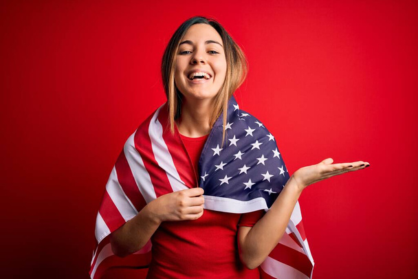 Joven hermosa rubia patriótica con ojos azules con bandera de los Estados Unidos muy feliz y emocionada, expresión ganadora celebrando la victoria gritando con una gran sonrisa y las manos levantadas
 - Foto, imagen