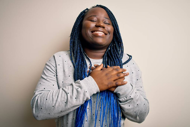 Afro-Amerikaanse plus size vrouw met vlechten dragen casual sweatshirt over een witte achtergrond glimlachen met handen op de borst met gesloten ogen en dankbaar gebaar op het gezicht. Gezondheidsconcept. - Foto, afbeelding