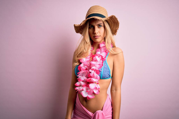 Jeune belle femme blonde en vacances portant un bikini et un chapeau avec des fleurs de lei hawaïennes sceptiques et nerveuses, fronçant les sourcils contrariés en raison de problèmes. Personne négative. - Photo, image