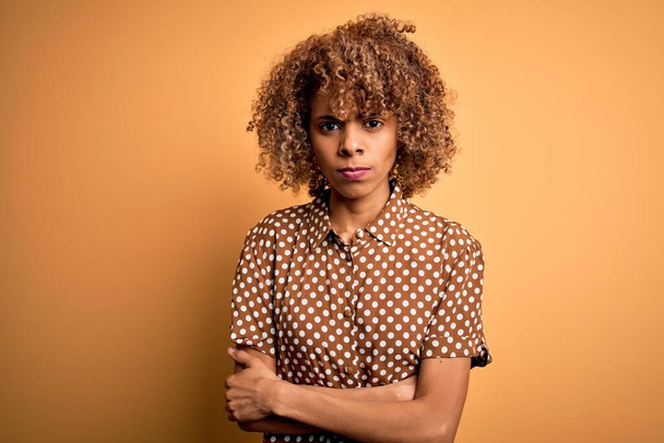 Fiatal, gyönyörű afro-amerikai nő alkalmi ingben áll sárga háttér szkeptikus és ideges, rosszalló kifejezés az arcon keresztbe tett karokkal. Negatív személy. - Fotó, kép